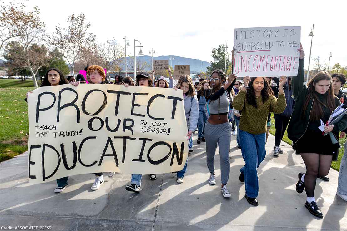 A group of students hold up signs in protest. The most prominent one reads in all caps, "Protect our education."