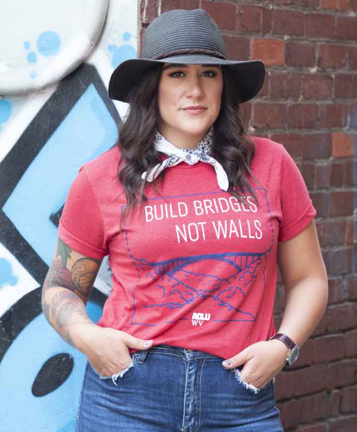 Model is pictured wearing a red Build Bridges Not Walls Tee Shirt showing the New river Gorge Bridge 