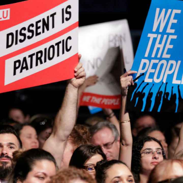 ACLU supporters hold signs that say "DISSENT IS PATRIOTIC" and "WE THE PEOPLE"