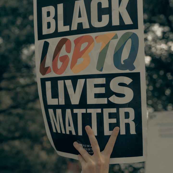 a hand holds a sign reading "Black LGBTQ Lives Matter"