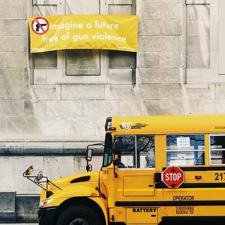 A school bus parked in front of a building carrying a yellow sign that says "Imagine a world free of gun violence."