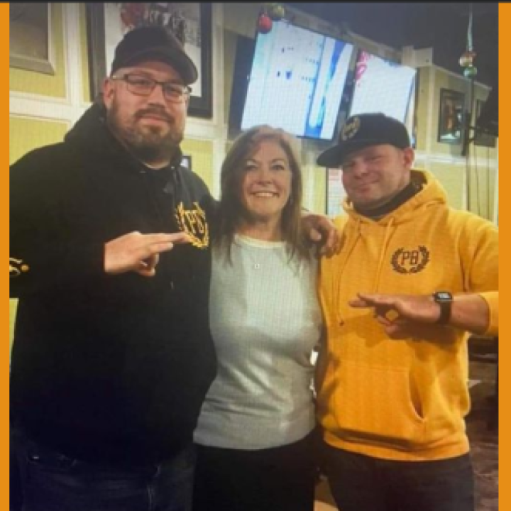 A Jackson County Commissioner stands between two men wearing Proud Boys-branded clothing as the men flash white power signs with their hands