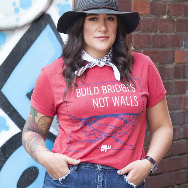 Model is pictured wearing a red Build Bridges Not Walls Tee Shirt showing the New river Gorge Bridge 